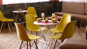 Un espace repas avec des chaises jaunes, des tables rondes et un banc.