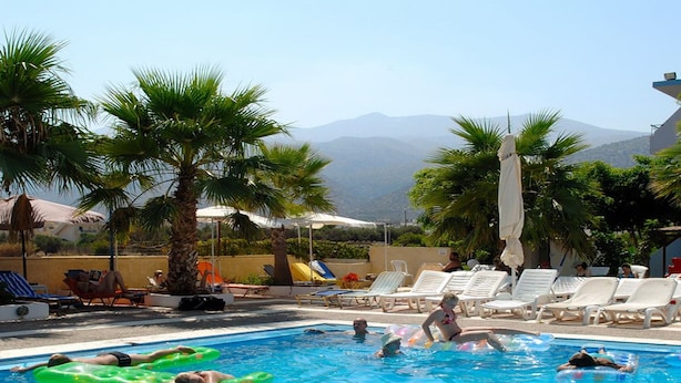 Une piscine où des personnes utilisent des bouées, entourée de palmiers et de chaises longues.