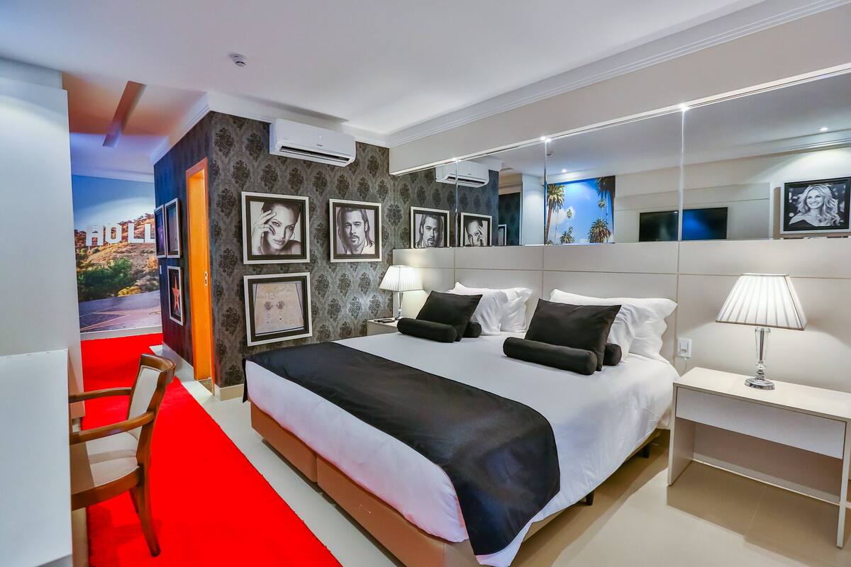 Een moderne hotelkamer met een groot bed, nachtkastjes, een bureau en een rood tapijt.