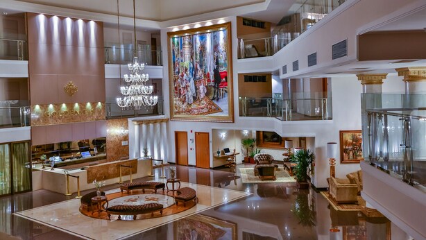 Eine mehrstöckige Hotelhalle mit einer zentralen Sitzecke, einem großen Wandgemälde und einer Rezeption.
