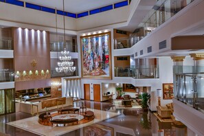 Un hall de hotel de varios niveles con una zona de estar central, un mural grande y una recepción.
