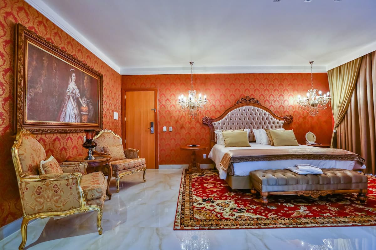 Een luxueuze slaapkamer met een groot bed, sierlijke stoelen, een kroonluchter en een rood betegeld tapijt.