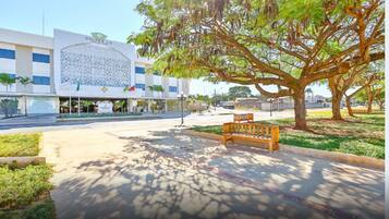 Un hotel con fachada moderna, un árbol grande al frente y un banco.