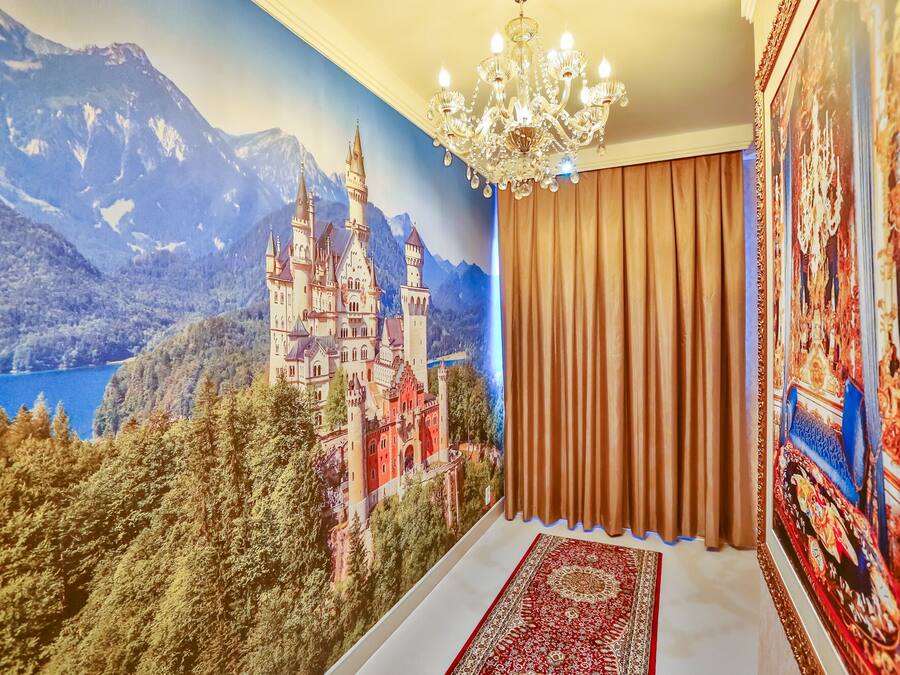 A room with a large mural of a castle, a chandelier, and a patterned rug.