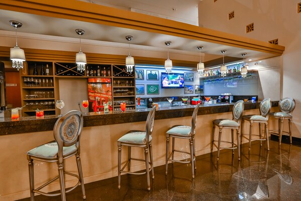Zona de bar con varios taburetes, estantes con botellas y una pantalla de televisión.