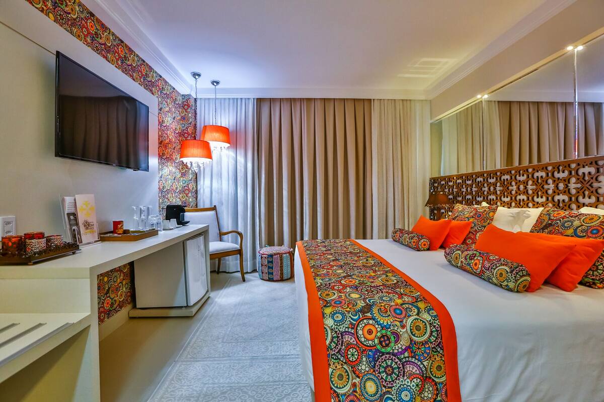 Een hotelkamer met een bed, een bureau, een stoel, een televisie en een gordijn met een patroon.