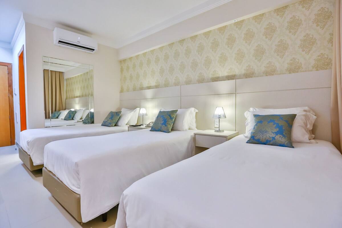 Een hotelkamer met twee bedden, een grote spiegel, een nachtkastje met een lamp en een wandairco.