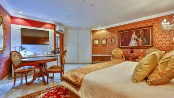 A hotel room with a bed, a desk, chairs, and a painting on the wall.