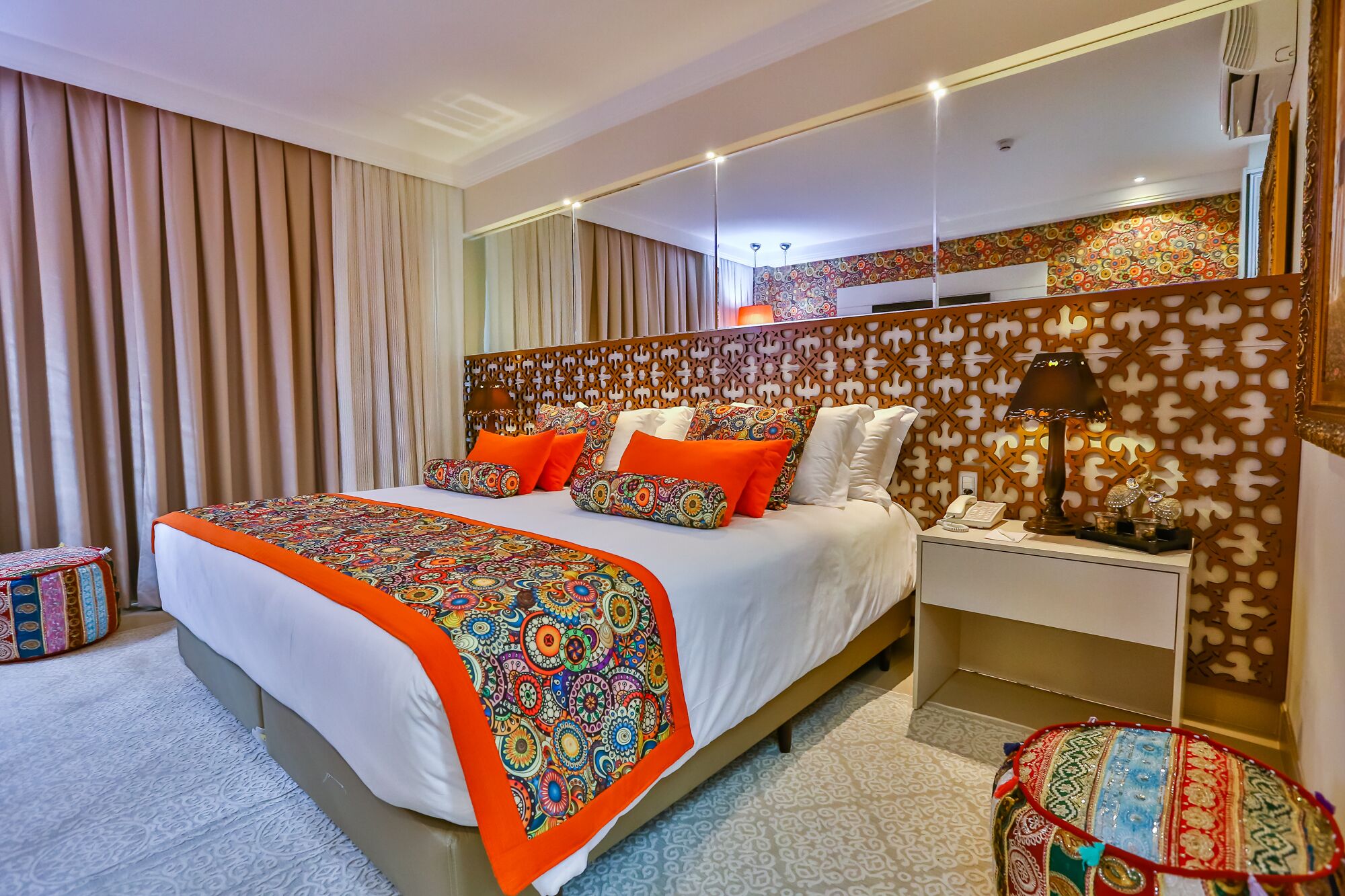 A hotel room with a large bed, a nightstand, a mirror, and a patterned headboard.