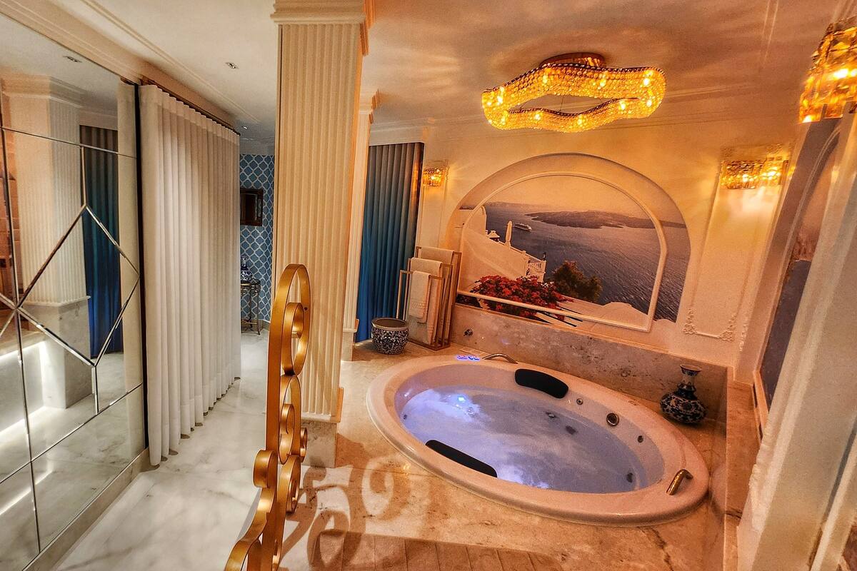 Een luxe badkamer met een groot bad, een spiegel met uitzicht en een modern design met marmeren vloeren en een geometrische spiegel.