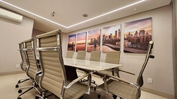 Un salón de conferencias con una larga mesa, cuatro sillas y cuadros con vistas a la ciudad.