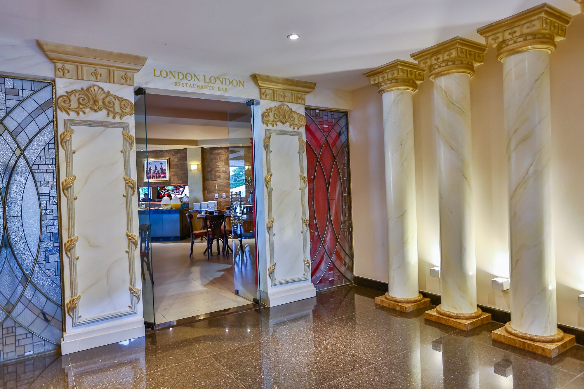 A grand entrance with marble columns and a glass door leading to a bar area with a cityscape view.