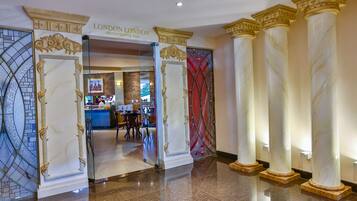 A grand entrance with marble columns and a glass door leading to a bar area with a cityscape view.