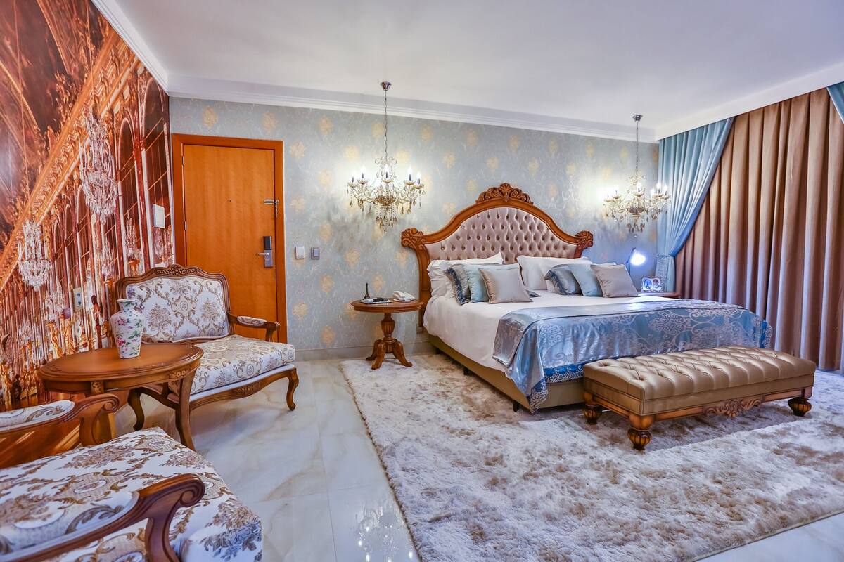 Een slaapkamer met een groot bed, een stoel, een tafeltje en een vloerkleed.