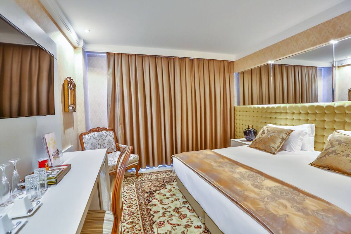 Een hotelkamer met een groot bed, een bureau met stoel, een spiegel en een raam met gordijnen.