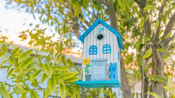 Een vogelhuisje met een blauw dak en witte muren, met een zonnebloem en een bordje waarop staat