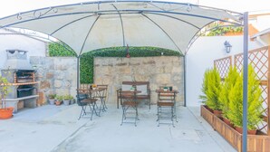 A covered patio area with stone walls, a grill, and potted plants. - Porto Island (Porto)