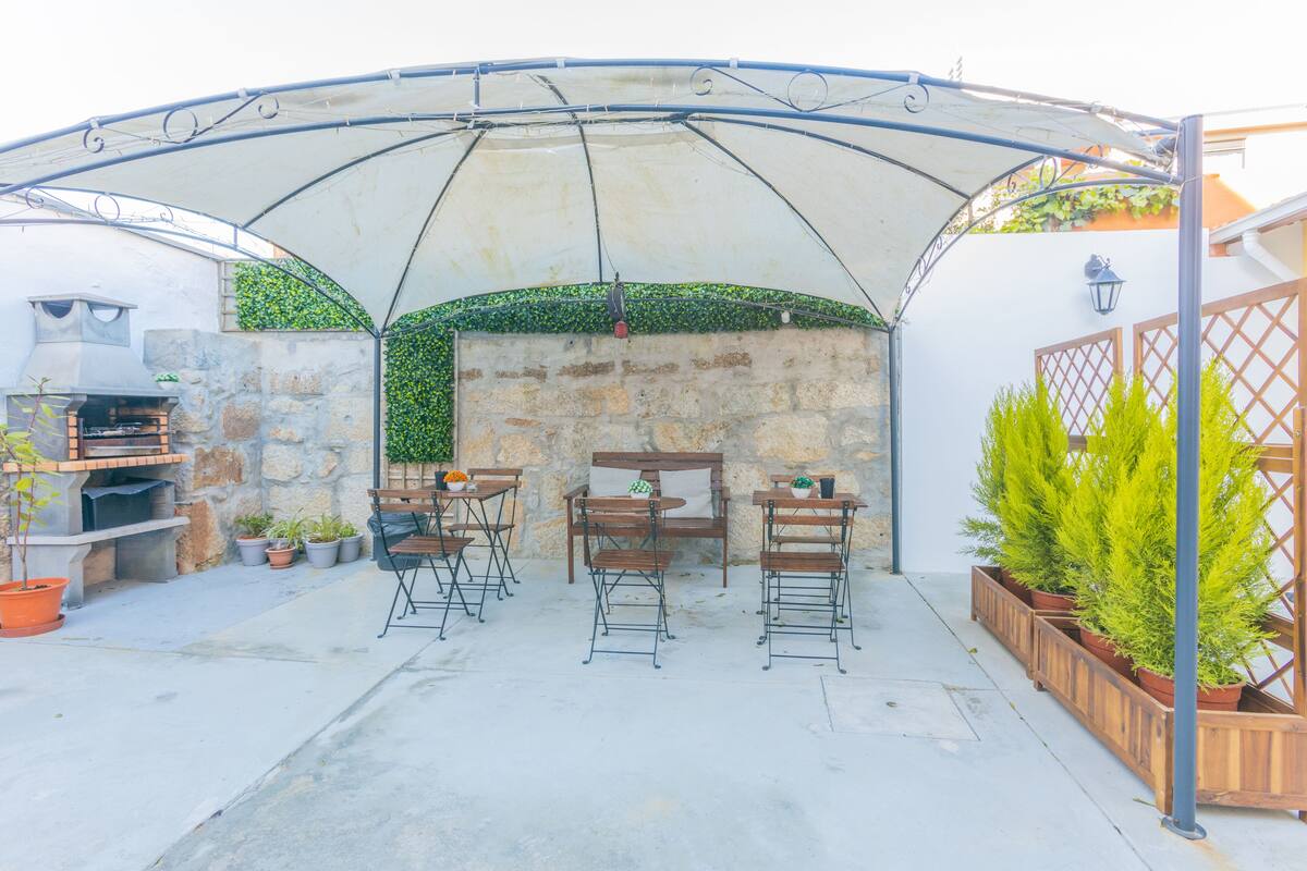 A covered patio area with stone walls, a grill, and potted plants.