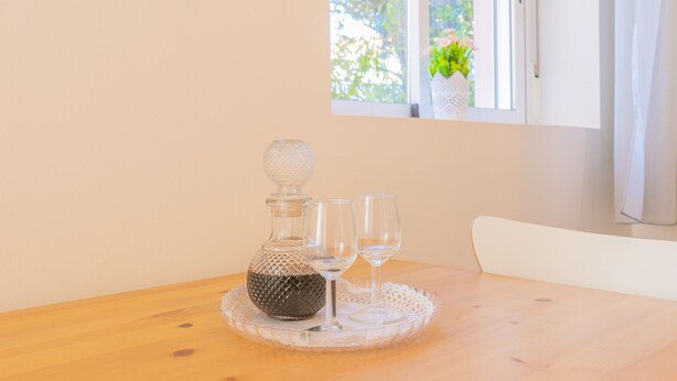 A wooden table with a glass decanter and two wine glasses on a lace doily. - Porto Island (Porto)