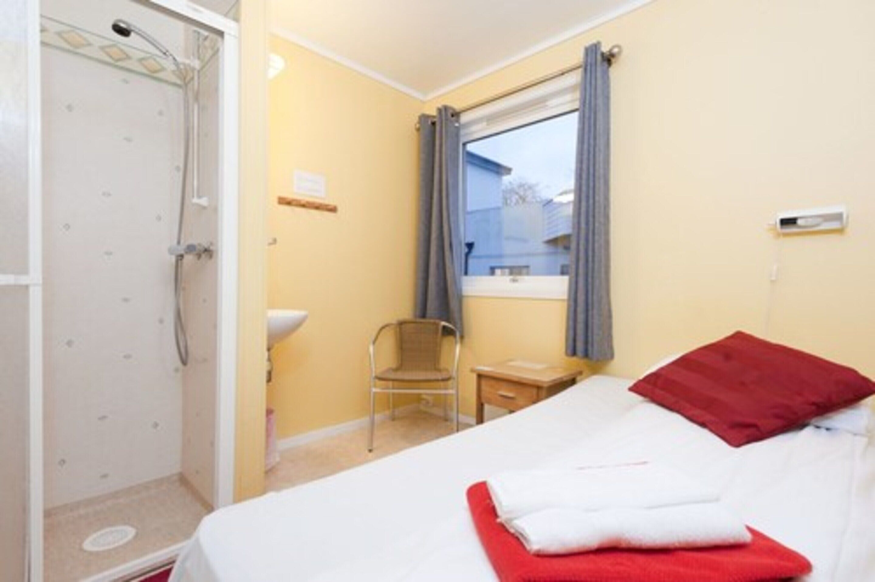 Une chambre d’hôtel comprenant un lit, une chaise, une petite table, une fenêtre avec des rideaux et un espace douche.