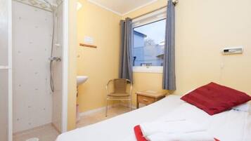 Une chambre d’hôtel comprenant un lit, une chaise, une petite table, une fenêtre avec des rideaux et un espace douche.