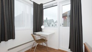 A room with a white desk, a chair, a window with curtains, and a view of buildings outside. - Stavanger Bed & Breakfast (Stavanger)