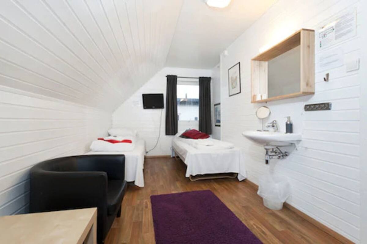 Una habitación pequeña y funcional con cama, escritorio, silla, lavabo y espejo.
