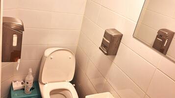 A bathroom with a toilet, a sink, a mirror, and a soap dispenser.
