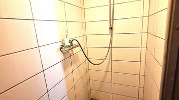 Un box de ducha pequeño con azulejos, un cabezal de ducha de mano y un grifo instalado en la pared.