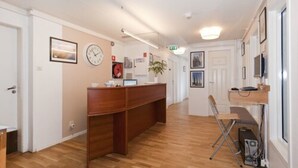 A reception area with a wooden desk, a clock, framed pictures, and a plant. - Stavanger Bed & Breakfast (Stavanger)