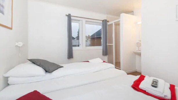 A hotel room with a bed, a window with curtains, a bedside table with a lamp, and a red blanket on the floor. - Stavanger Bed & Breakfast (Stavanger)