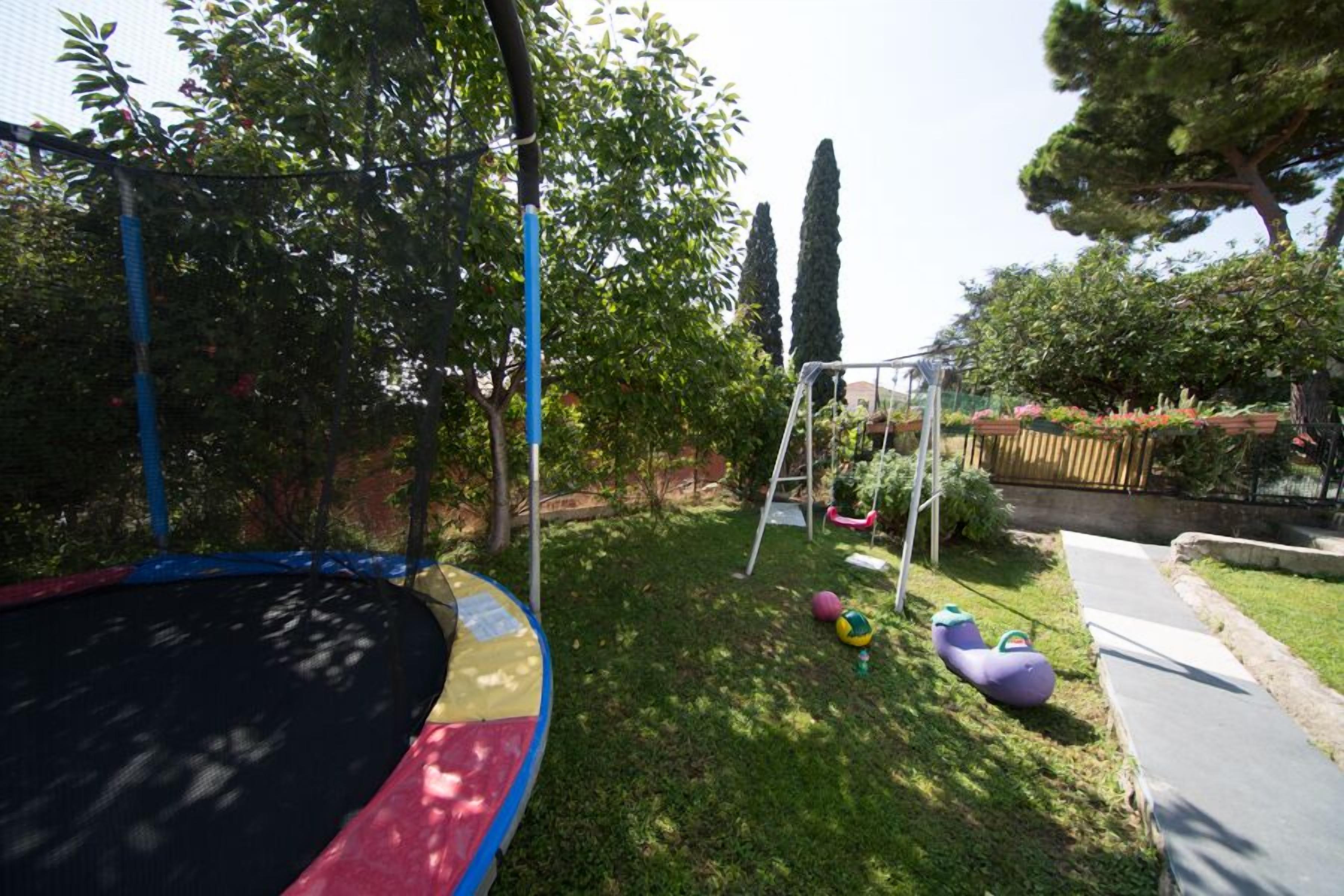 A backyard with a trampoline, a swing set, and a small garden area.