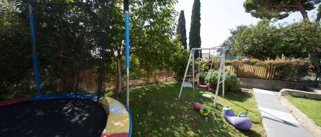 A backyard with a trampoline, a swing set, and a small garden area.