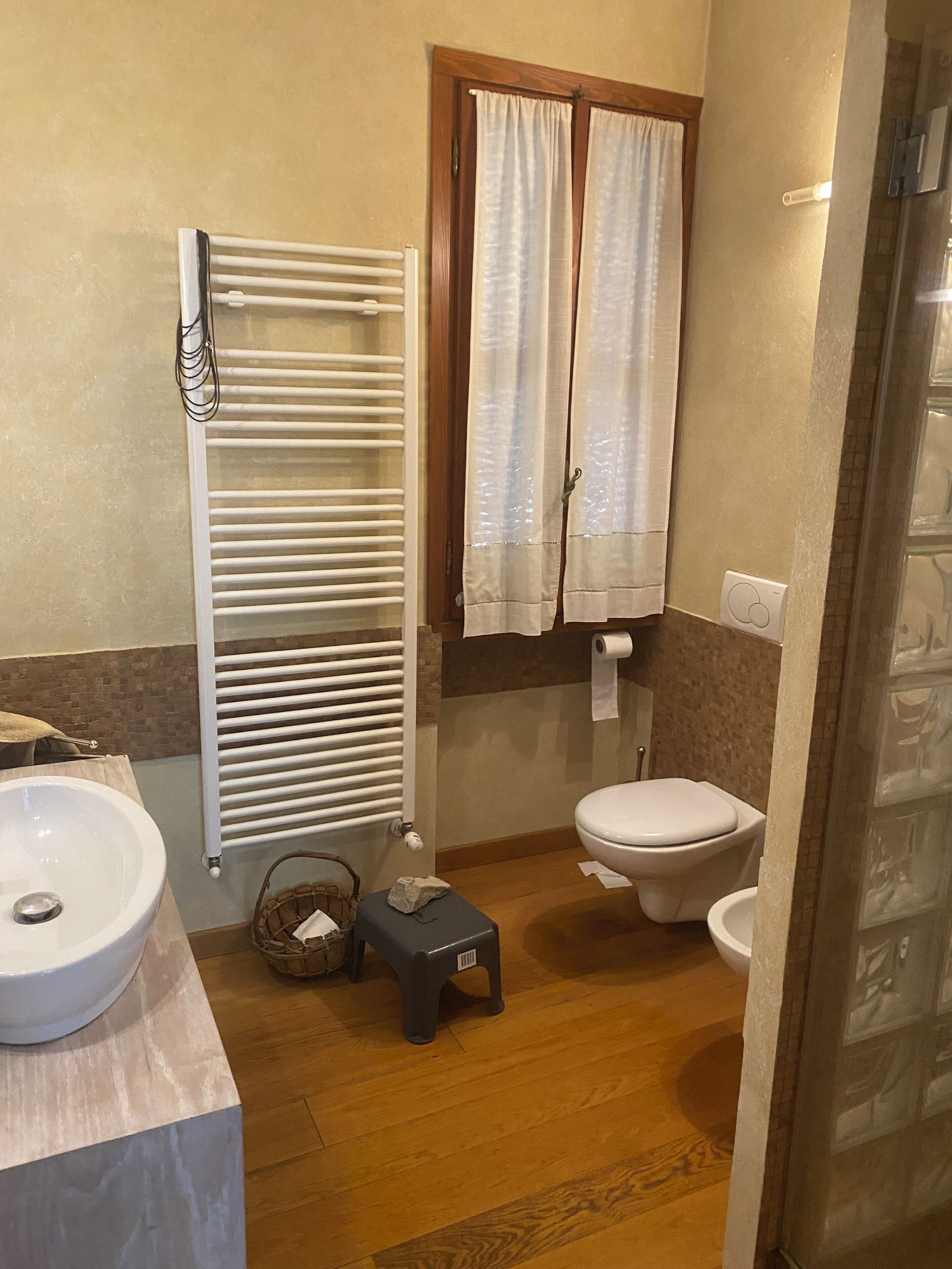 A bathroom with a white sink, a toilet, a radiator, and a window with curtains.