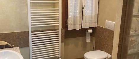 Un baño con lavamanos blanco, inodoro, radiador y ventana con cortinas.