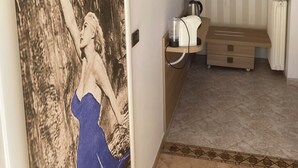 A hotel room with a striped wall, a wooden bench, a radiator, and a small shelf with clothes and a kettle. - La Dolce Vita (Taggia)