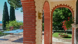 A brick archway leading to a patio area with a table and chairs, surrounded by greenery and a view of the sea. - La Dolce Vita (Taggia)