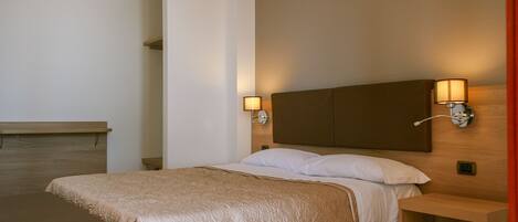 A hotel room with a bed, bedside tables, and wall-mounted lamps.
