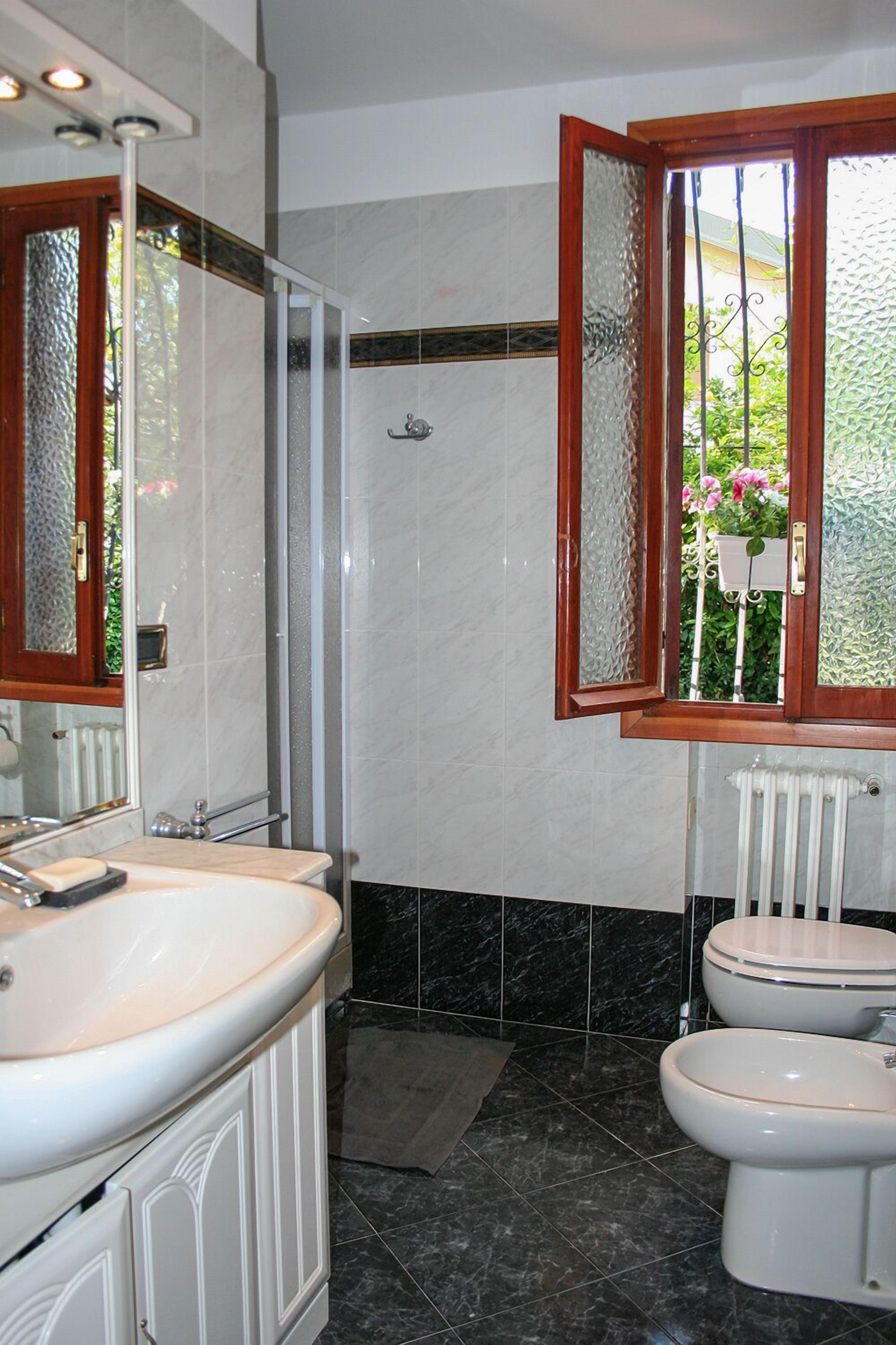 Une salle de bain avec un lavabo blanc, des toilettes et une douche. Il y a une fenêtre avec un cadre en bois et du verre dépoli.