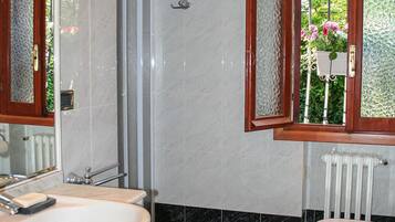 Baño con lavamanos blanco, inodoro y ducha. Cuenta con un ventanal de madera con vidrio satinado.