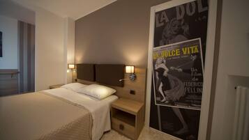 A hotel room with a bed, bedside lamps, a poster on the wall, and a wooden nightstand.