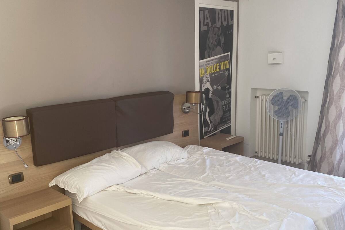 A bedroom with a bed, bedside tables, a wall-mounted light, a poster, and a radiator.