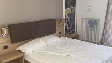 A bedroom with a bed, bedside tables, a wall-mounted light, a poster, and a radiator.