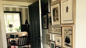 Un pasillo con una puerta oscura, un comedor con mesa y sillas, y una pared decorada con cuadros.