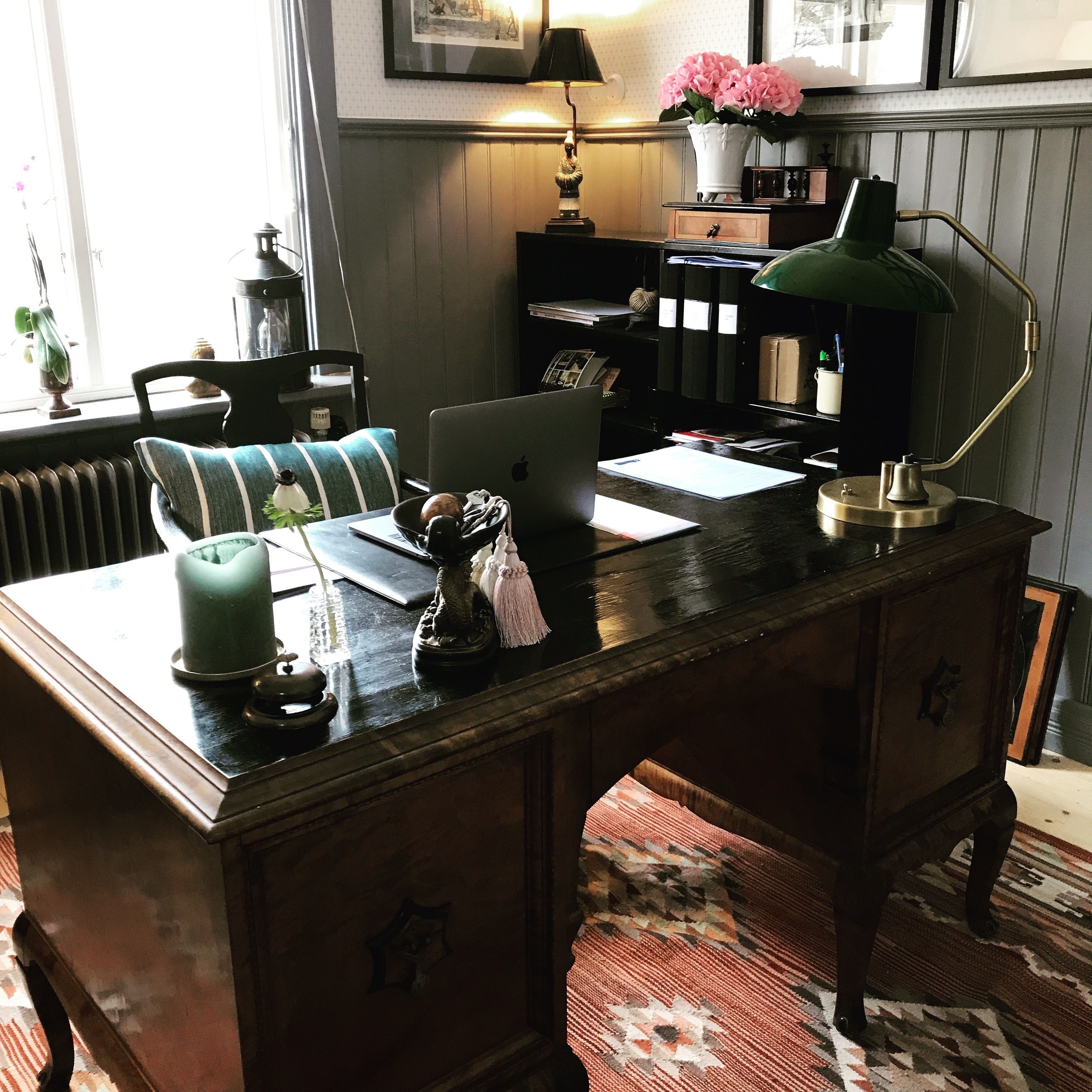 A wooden desk with a laptop, a green desk lamp, and various decorative items.