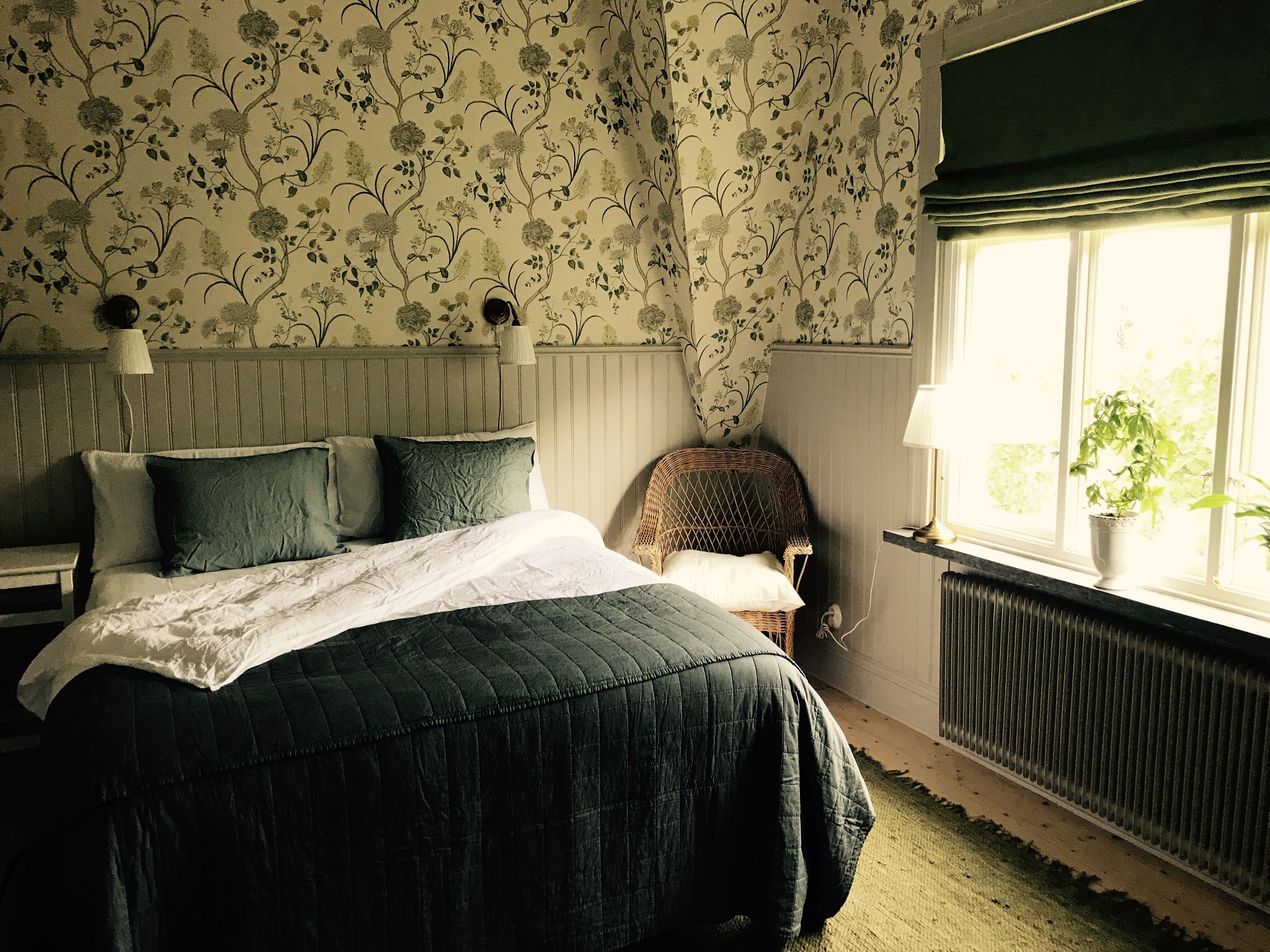 A bedroom with a bed, a chair, a window with a plant, and a radiator.