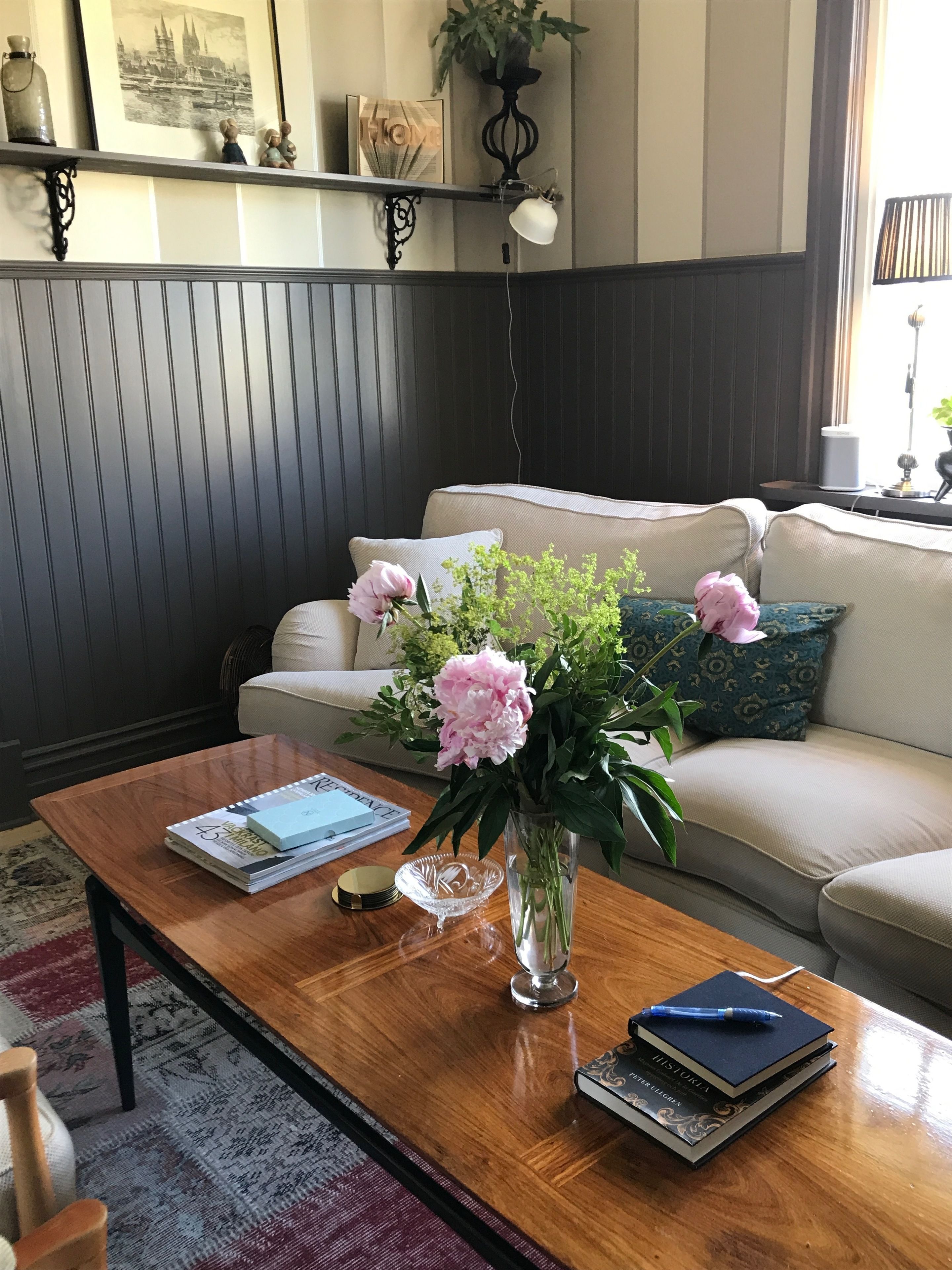 A living room with a wooden coffee table, a sofa, a bookshelf, and a vase with flowers.