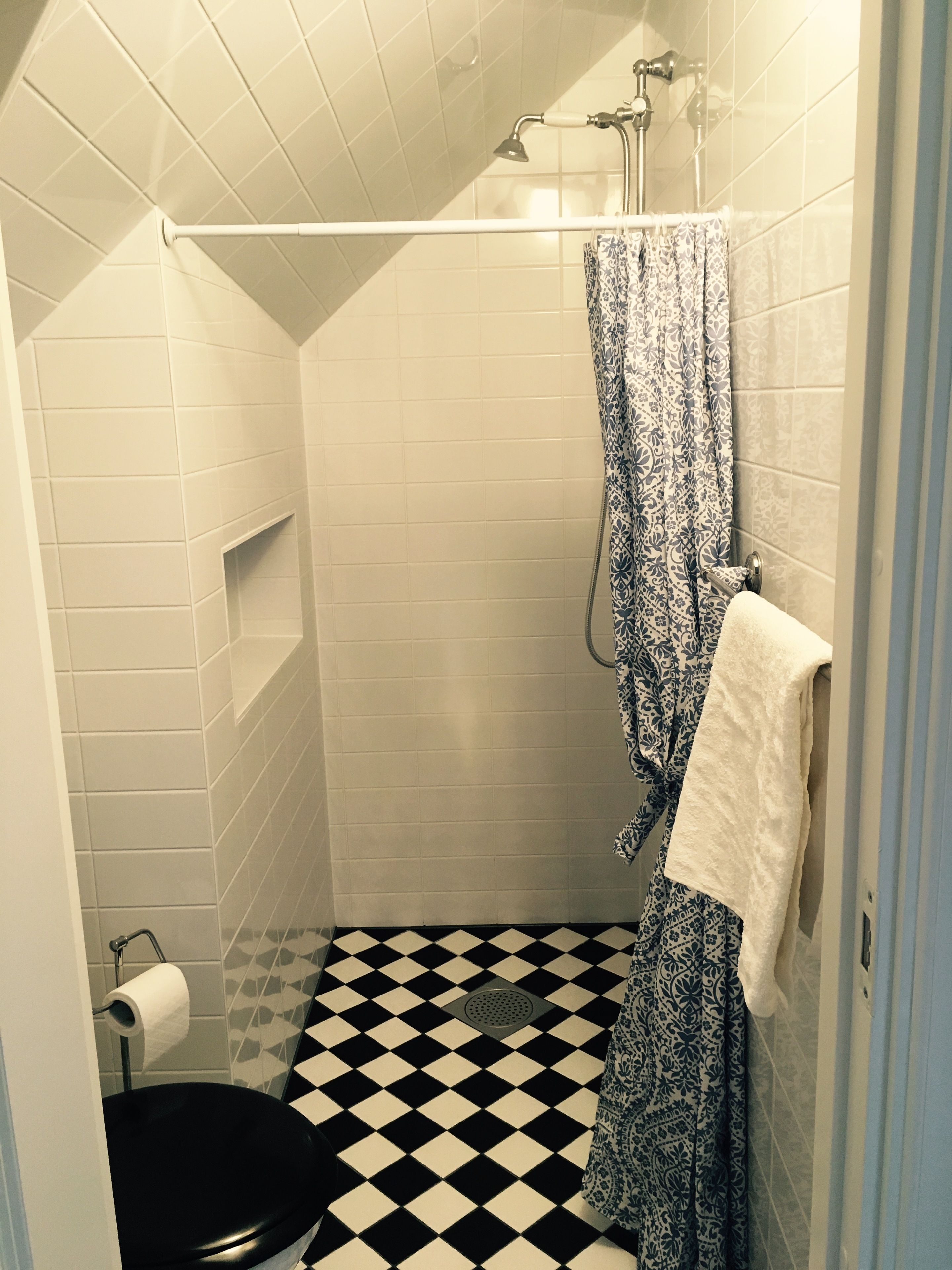 Une petite salle de bain carrelée, avec une douche, des toilettes et une serviette à motifs accrochée au mur.