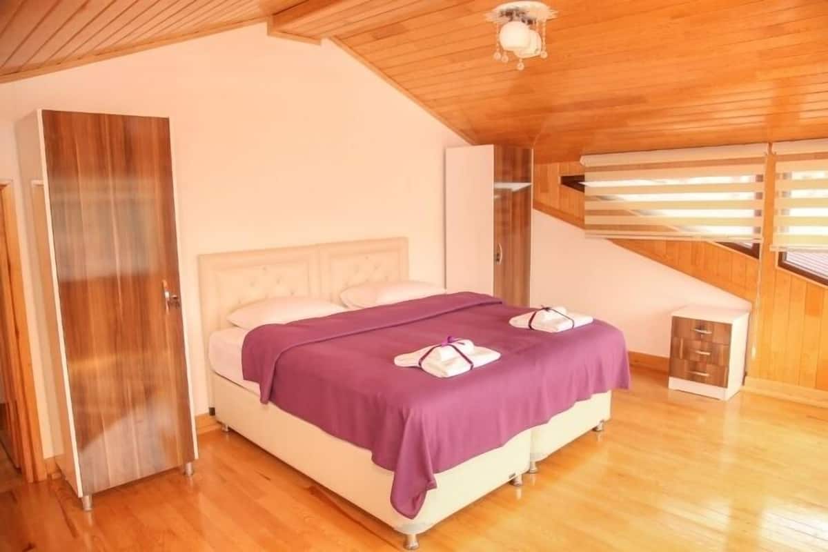 A bedroom with a wooden ceiling, a bed with a purple bedspread, and a small bedside table.
