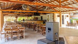 Un espace de restauration en plein air avec des tables et des chaises en bois, un bar central et une structure de toit abritée.